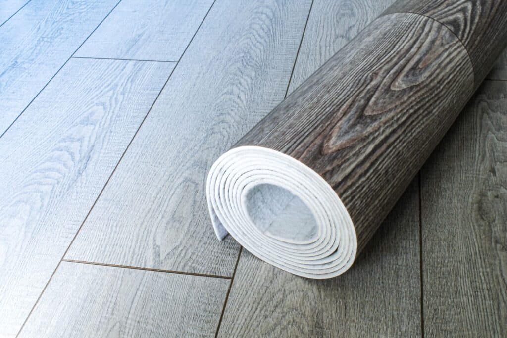 Smooth grey and brown wood-effect flooring planks with a rolled white underlay for premium garden room flooring solutions.
